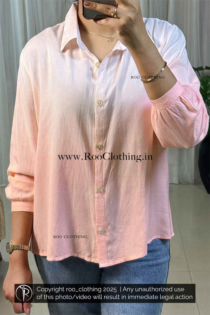 Person wearing a light pink shirt with rolled-up sleeves, taking a mirror selfie.