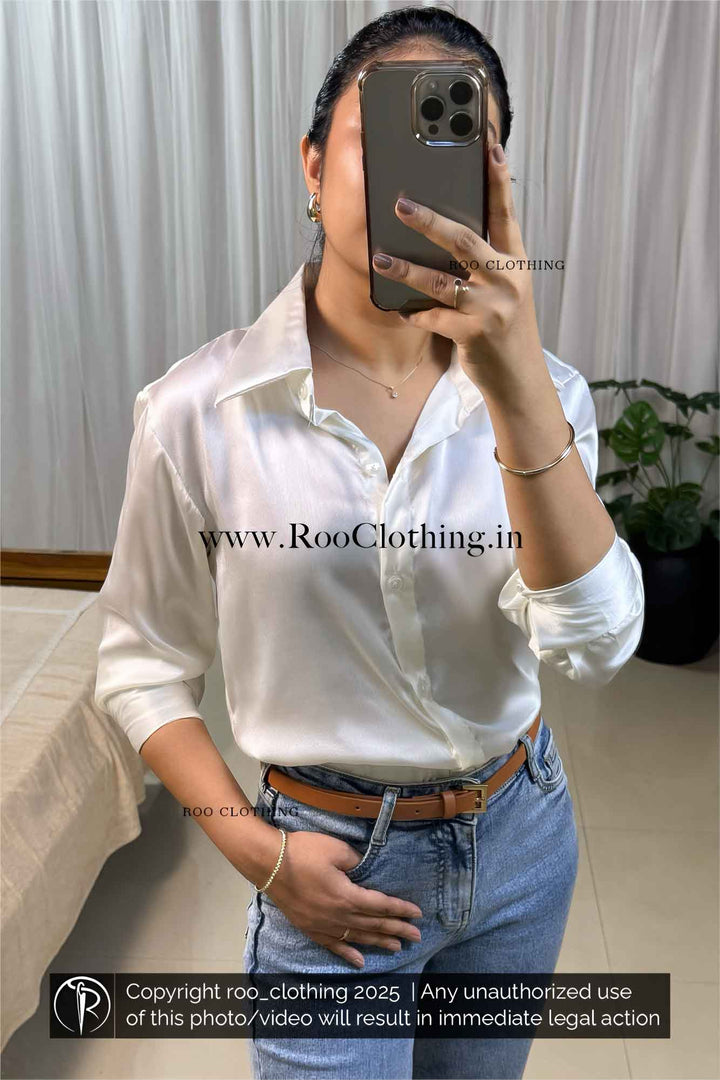 Person wearing a white shirt and blue jeans, holding a phone with a blurred face.