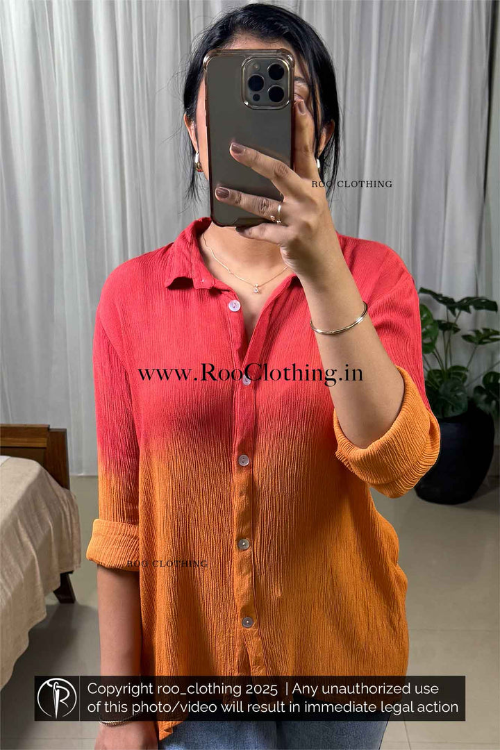 Person wearing a red and orange shirt taking a mirror selfie with a blurred background.