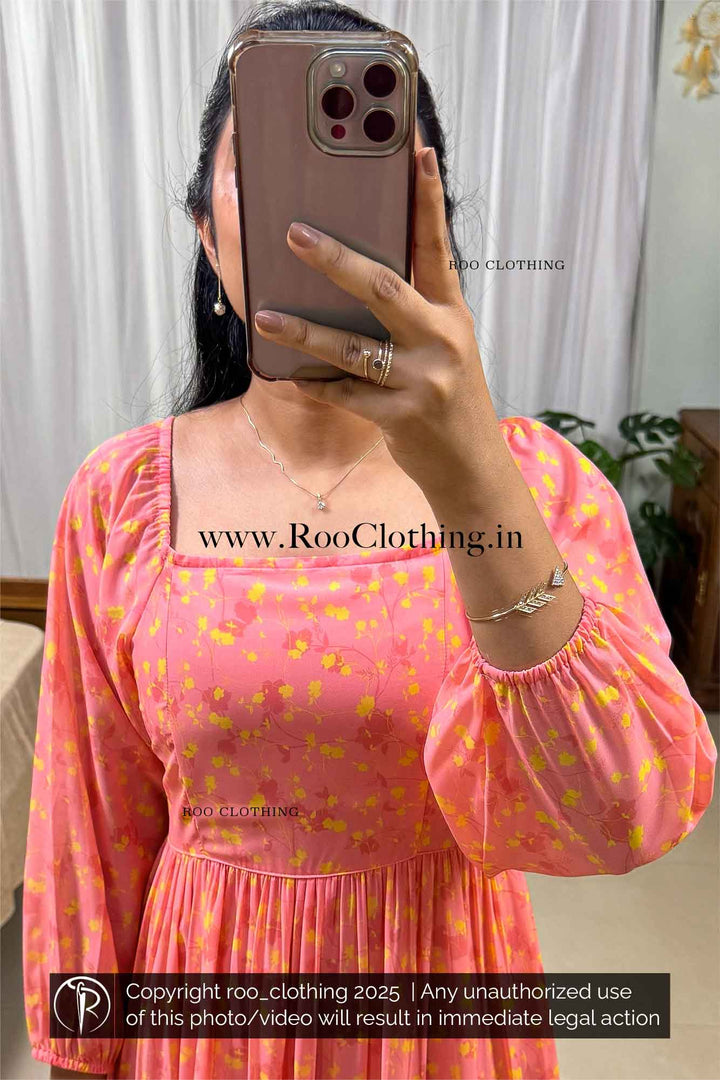 Woman wearing a peachy tangerine tiered midi dress made of lightweight georgette, featuring  raglan armholes, Wide round neckline, 3/4th length balloon sleeves with elasticated cuffs, Elasticated smocking at the back bodice, and soft butter crepe lining – Roo Clothing
