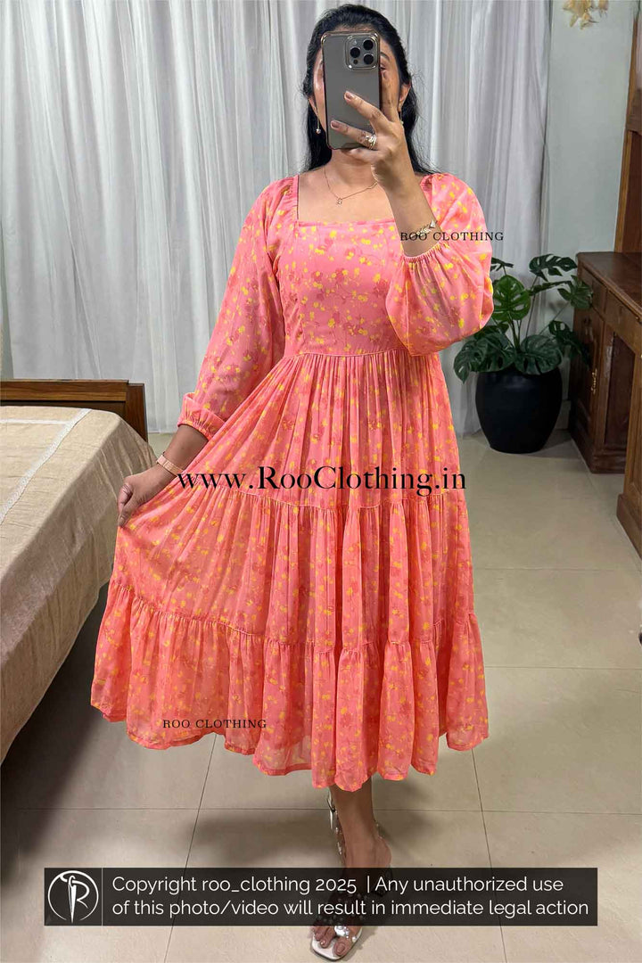 Woman wearing a peachy tangerine tiered midi dress made of lightweight georgette, featuring  raglan armholes, Wide round neckline, 3/4th length balloon sleeves with elasticated cuffs, Elasticated smocking at the back bodice, and soft butter crepe lining – Roo Clothing